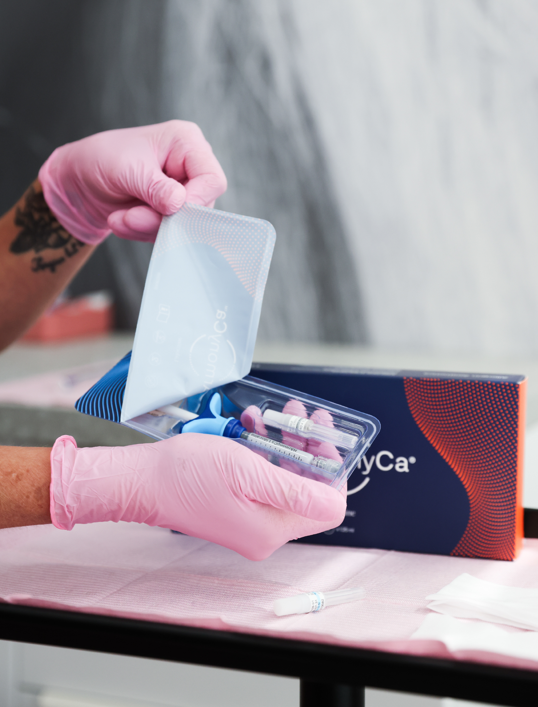 Professionnelle en gants roses présentant une trousse de traitement HArmonyCa contenant une seringue dans un environnement médico-esthétique.