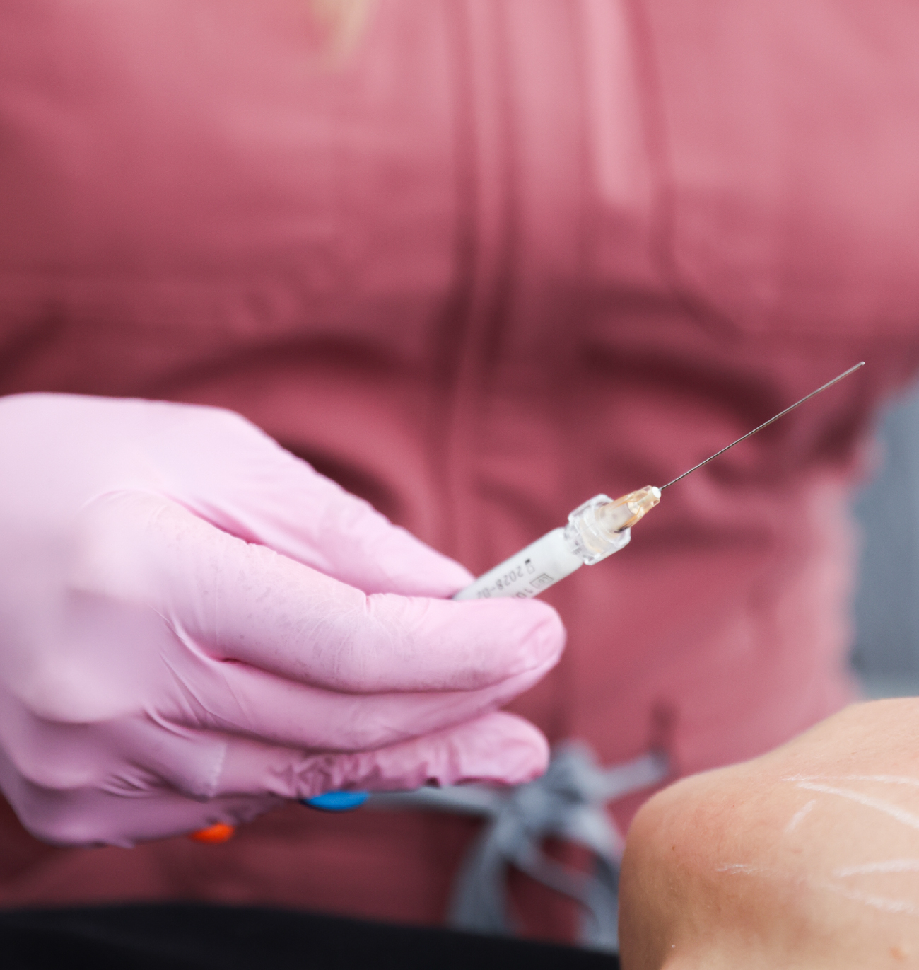 Professionnelle en gants roses tenant une seringue d’injection esthétique près du visage d’une patiente.