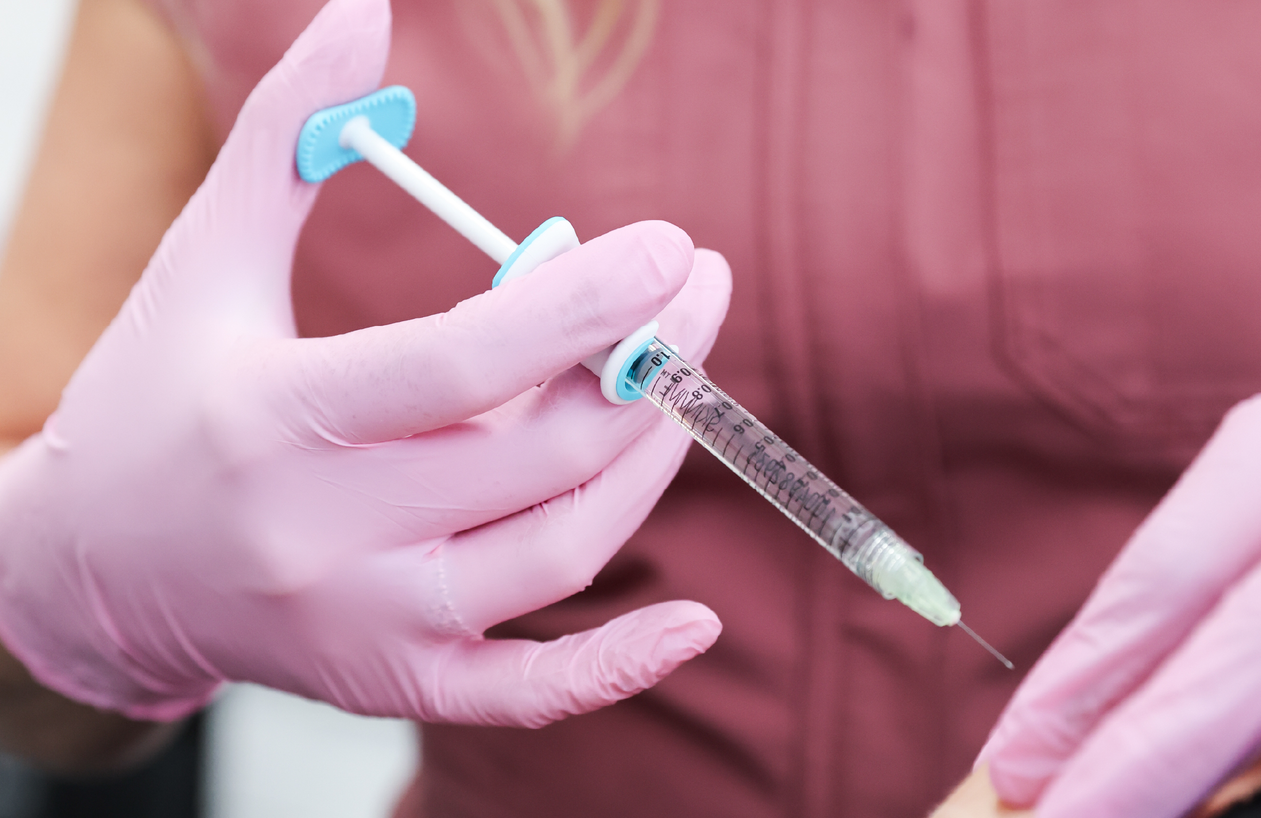 Professionnelle de la médecine esthétique portant des gants roses et tenant une seringue utilisée pour un traitement injectable Skinvive.